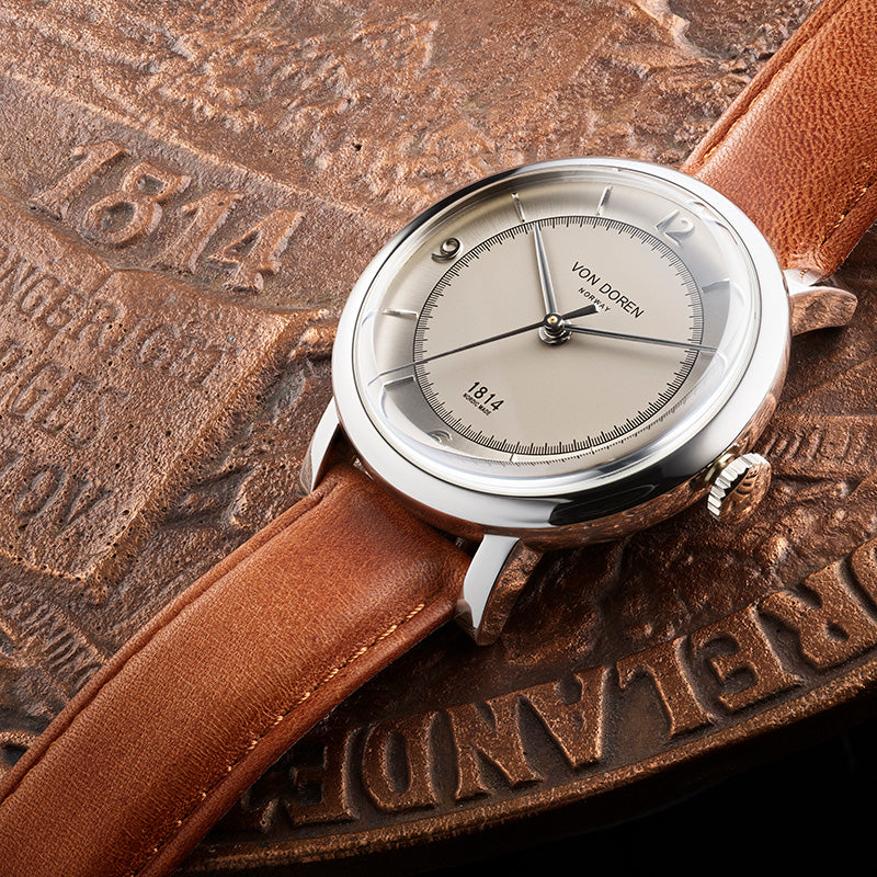 Von Doren 1814 with light dial and brown leather strap resting on a historic Eidsvoll medallion from 1814.