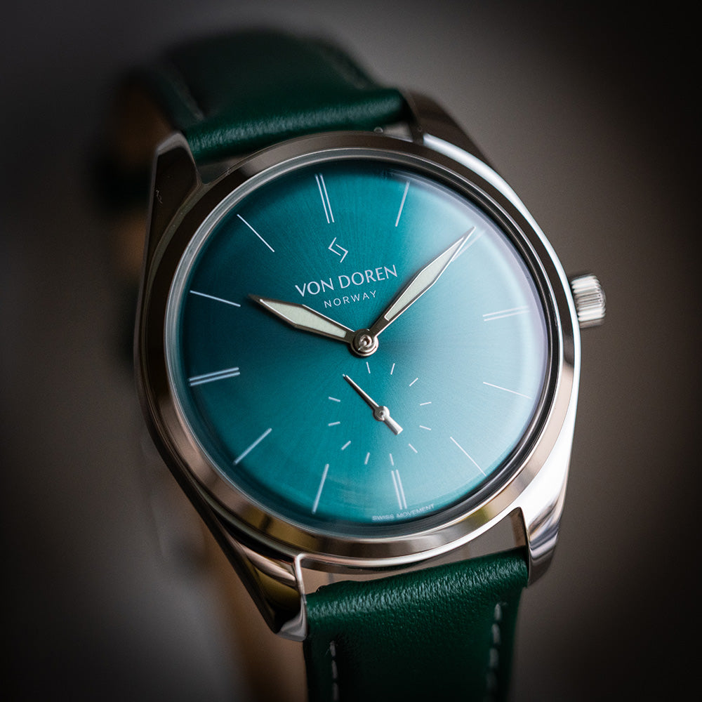 Von Doren Runde Opal. Klokken har stålkasse, grønn skive, sorte indekser og grønn skinnreim med hvite sting.
