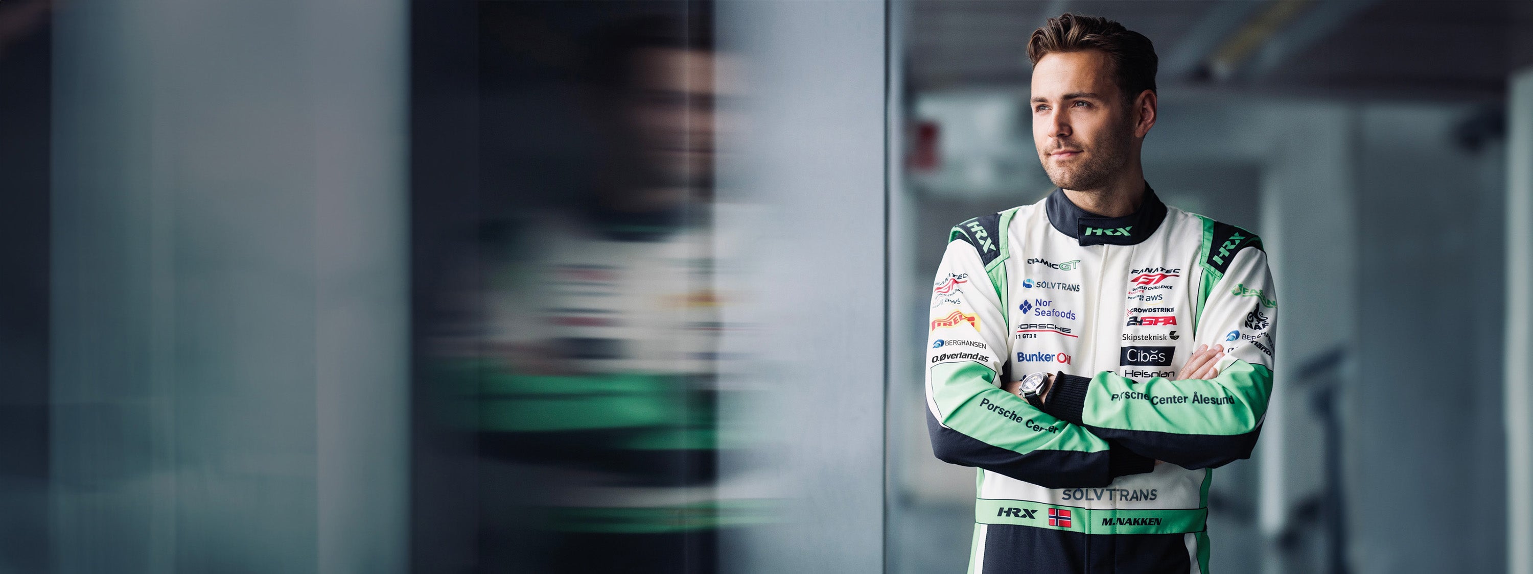 Racing driver Marius Nakken in his Porsche race suit standing with arms crossed.
