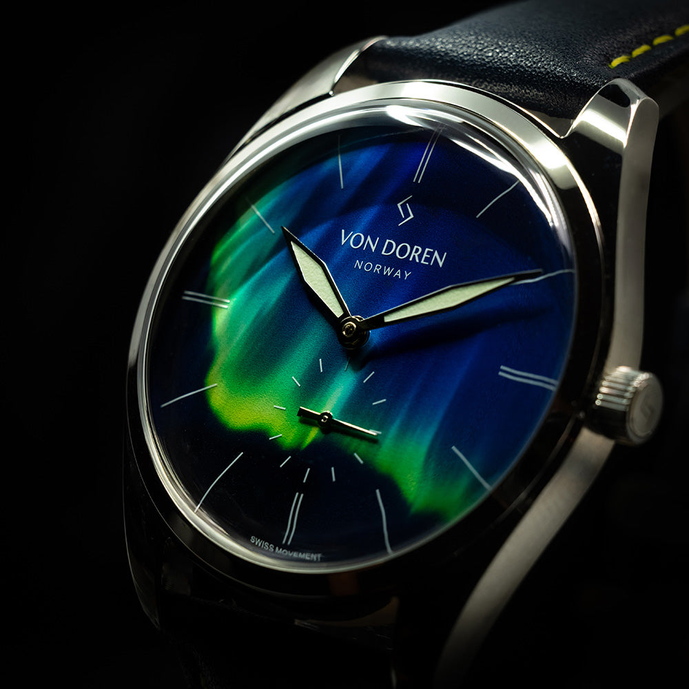 Nærbilde av Von Doren klokkevisere med grønt lume over nordlys urskiven.