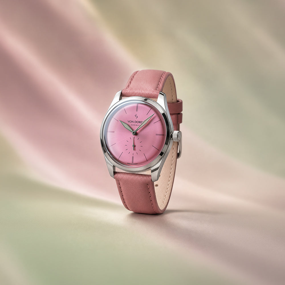 Von Doren-klokke med rosa skive og rosa skinnrem med dus bakgrunn i rosa og grønn.