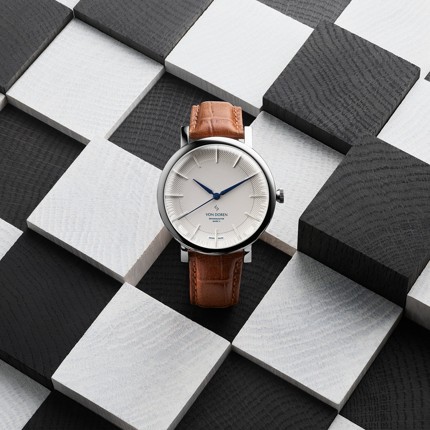 Von Doren-klokke med hvit tallskive og brun rem på svart-hvitt mønster.