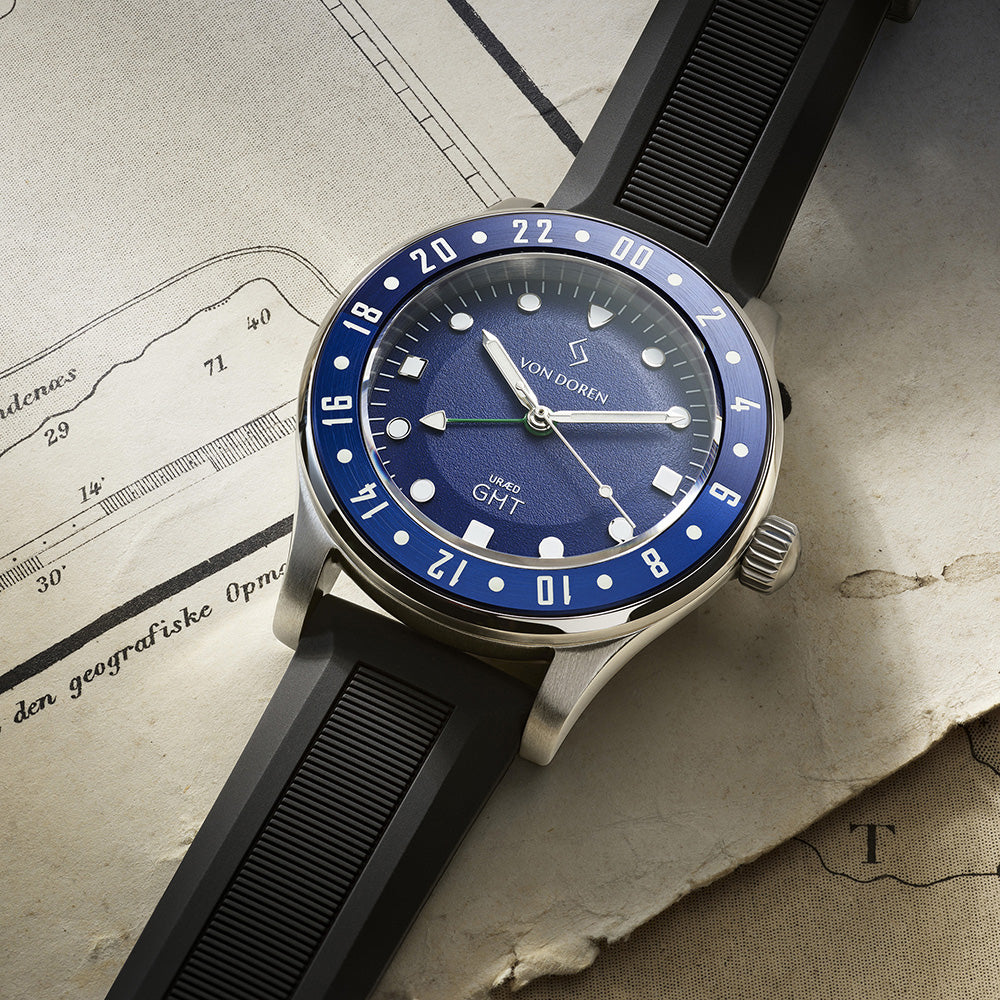 Klokke med blå skive og sort reim ligger på et gammelt kart