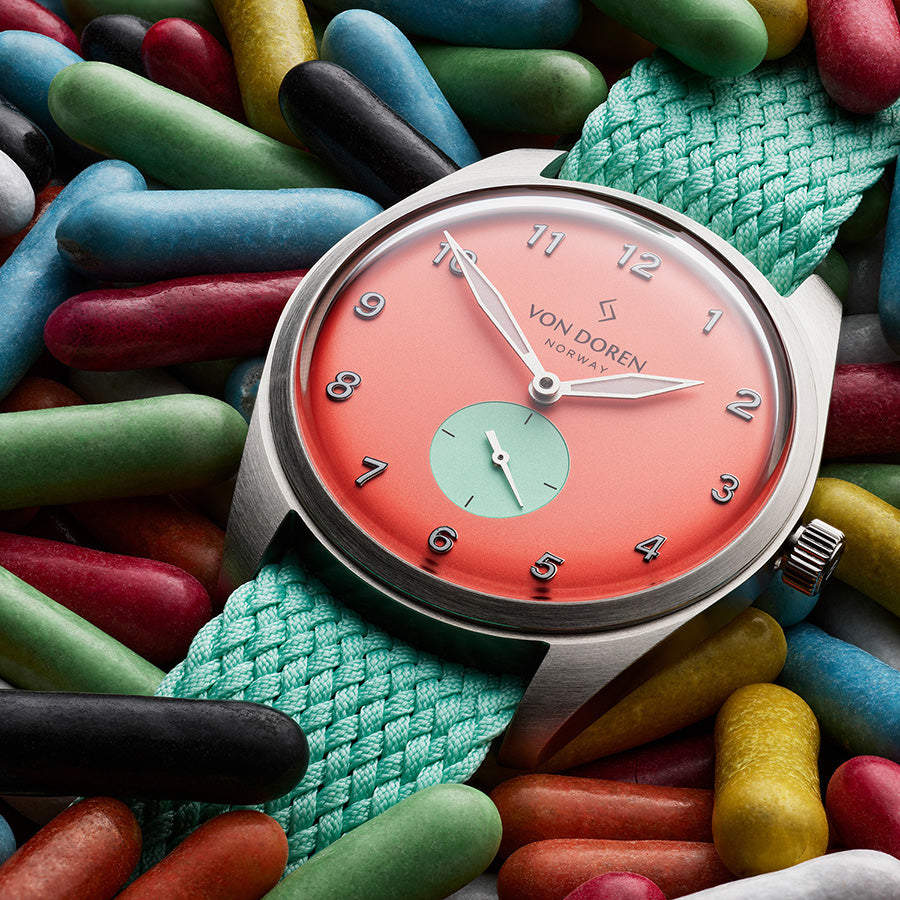 Chillirød klokke med grønn perlonstrap, liggende oppå godterier